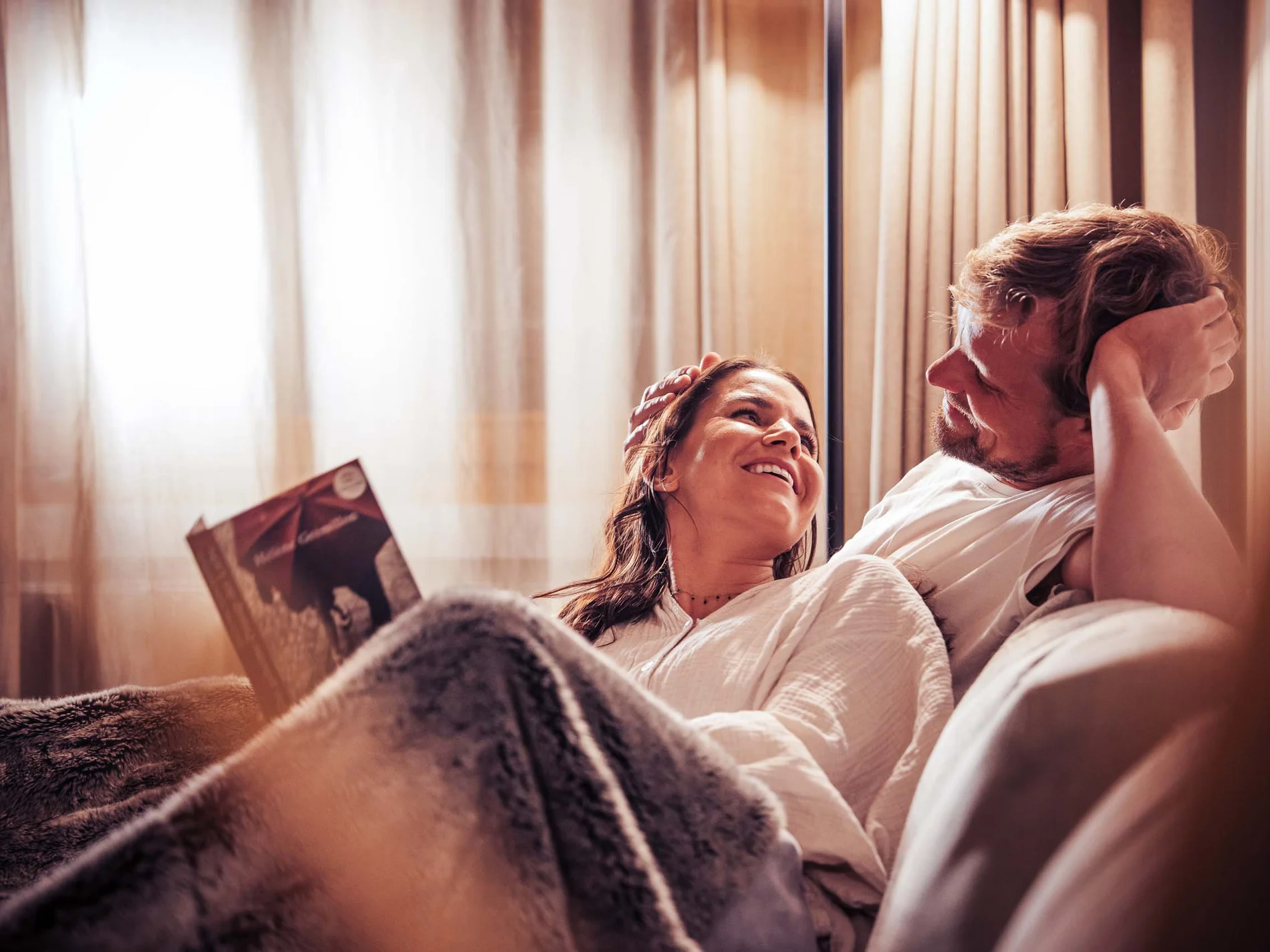 Paar kuschelt auf der Couch unter Decke, Frau hält Buch in der Hand