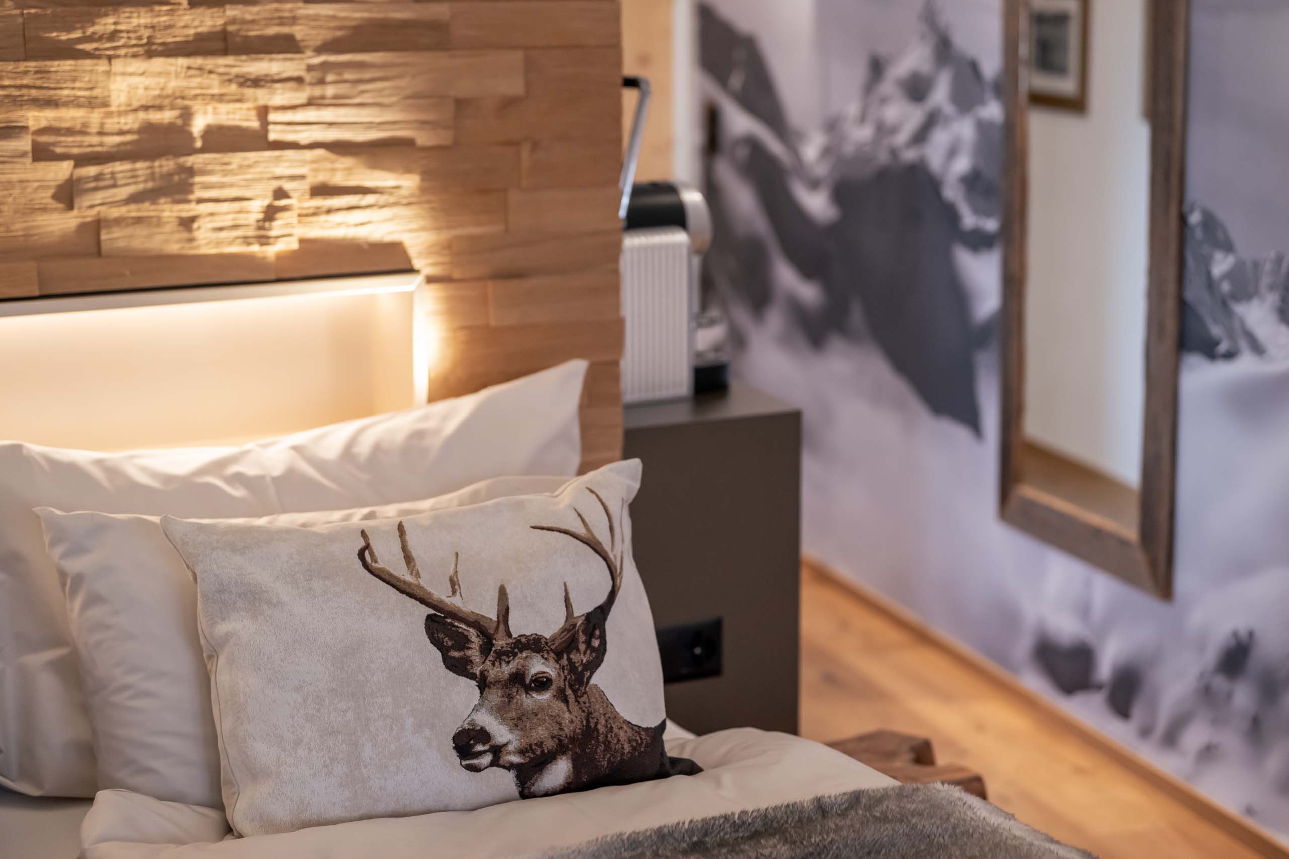 Kissen mit Hirschmotiv auf einem Bett vor einem beleuchteten Holzpaneel