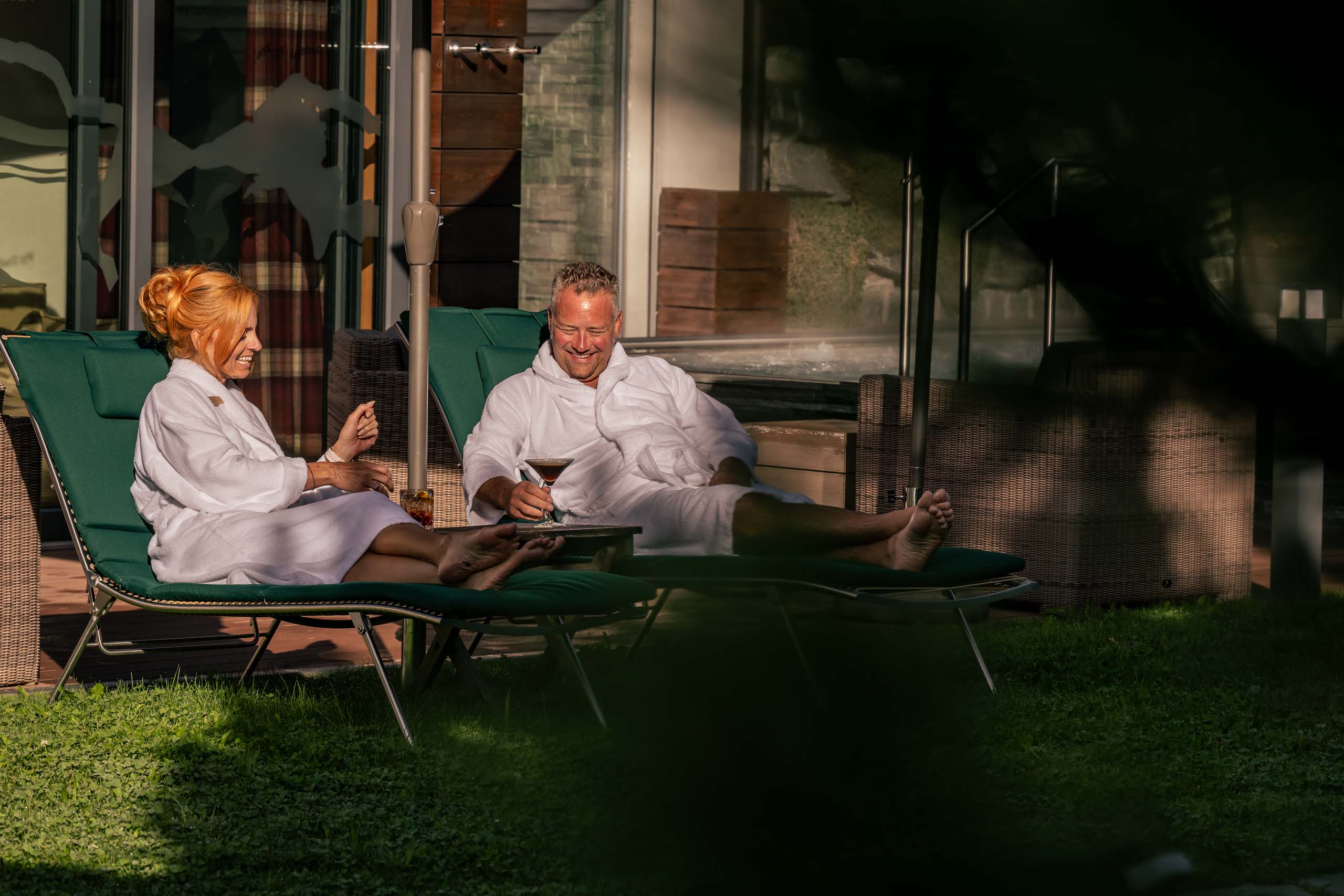 Paar entspannt im Bademantel auf Liegestühlen mit Getränken im Freien